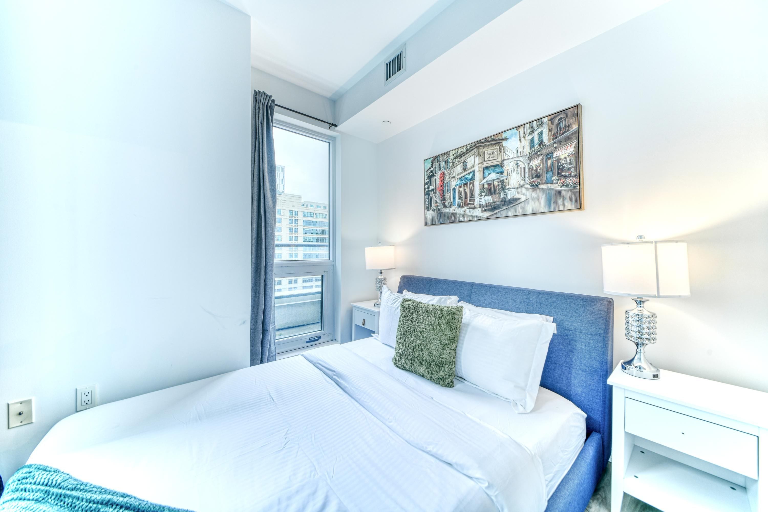 A hotel room with a large bed, a nightstand, a lamp, and a window with curtains.