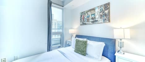 Una habitación de hotel con una cama grande, una mesita de noche, una lámpara y una ventana con cortinas.
