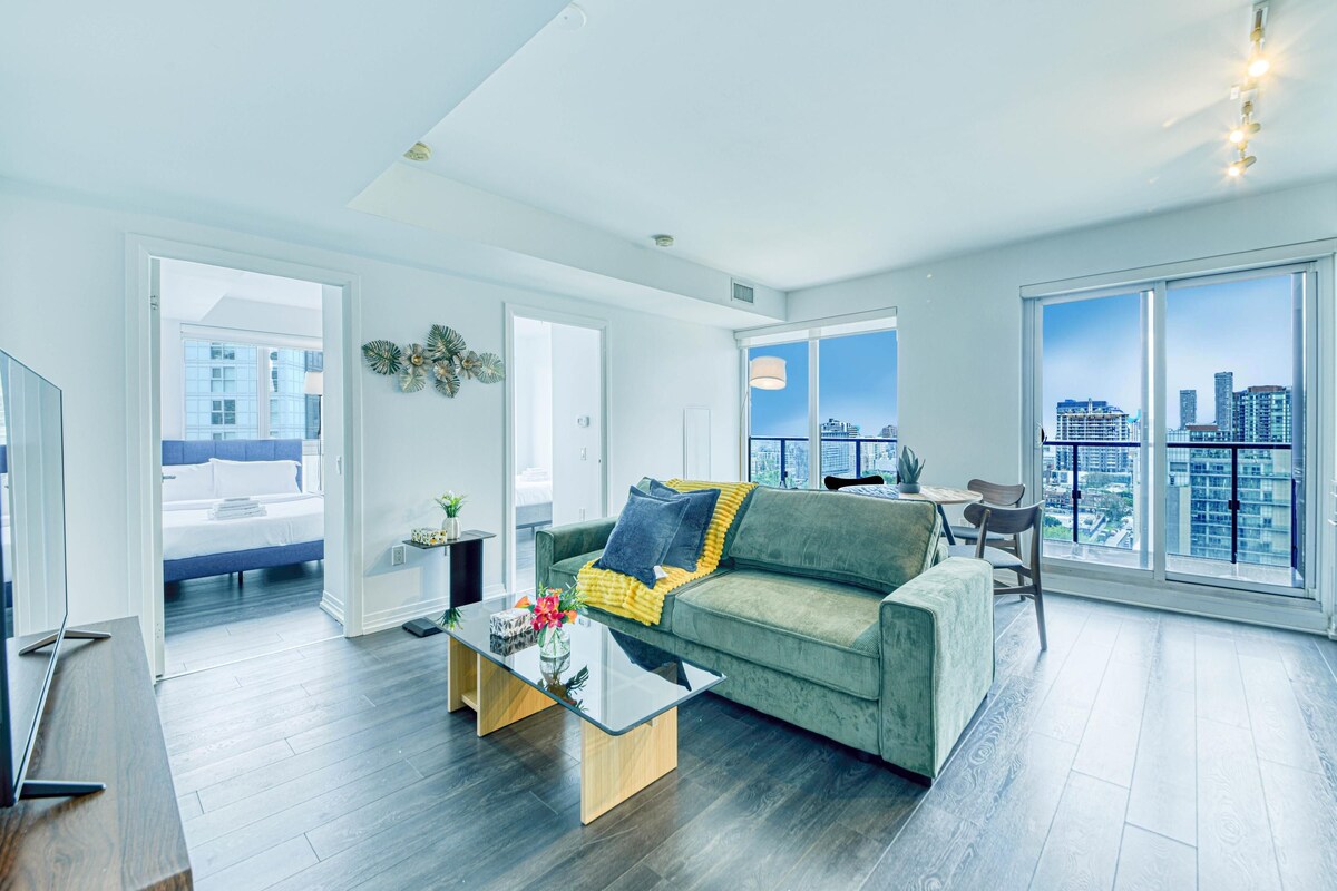 A modern living room with a green sofa, a glass coffee table, and a city view through large windows.