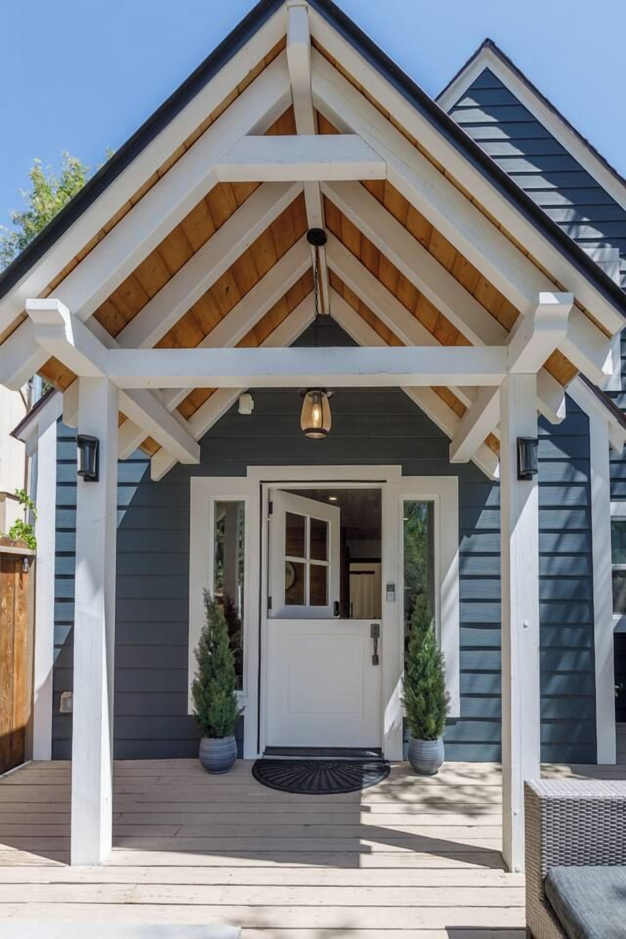 Une maison avec un porche couvert, une porte d’entrée et deux plantes en pot.