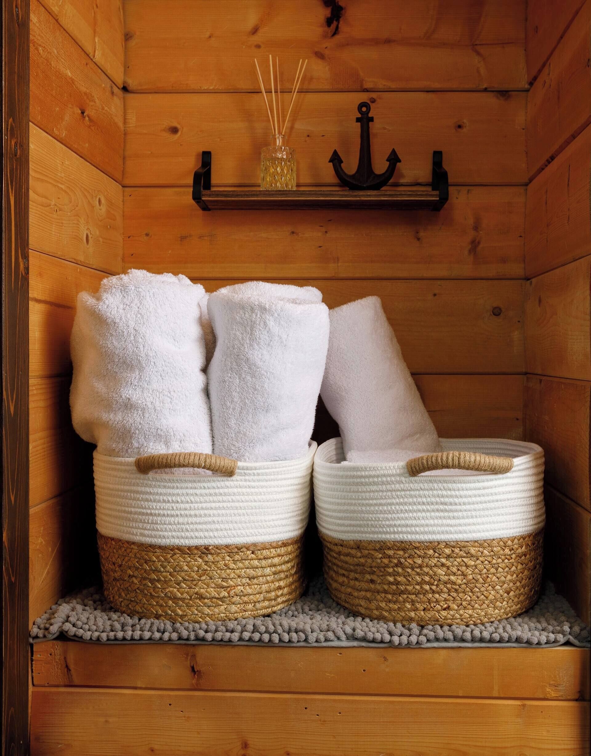 Two woven baskets with white towels on a shelf in a wooden room.