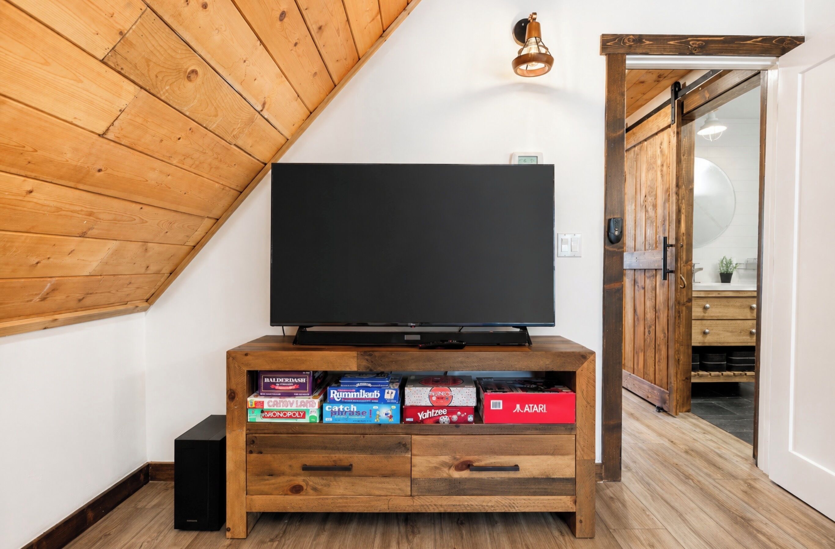 Un meuble de rangement en bois comprenant un téléviseur à écran plat, des tiroirs et une étagère où sont rangés des jeux de société.