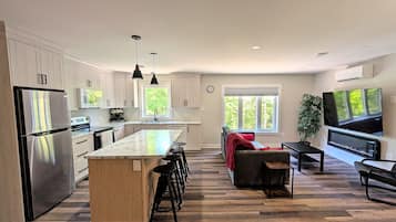 A modern kitchen with a central island, stainless steel appliances, and a dining area with a TV and seating.