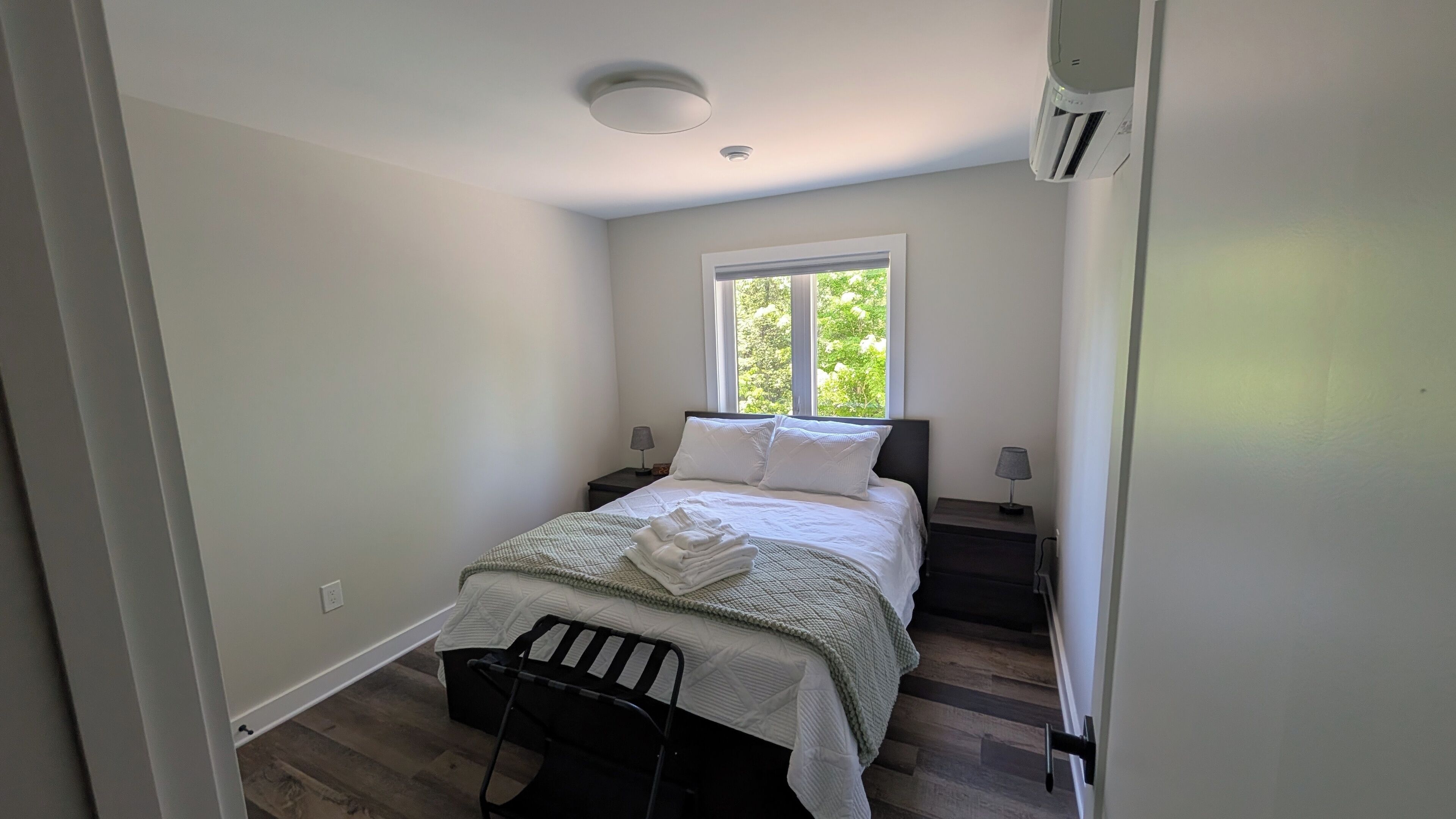 Une chambre à coucher avec un lit, une fenêtre, une table de chevet, une lampe et une chaise.