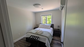 A bedroom with a bed, a window, a nightstand, a lamp, and a chair.