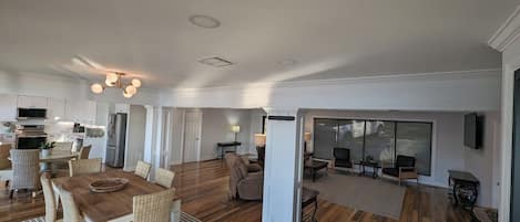 Uma sala de estar ampla com piso de madeira, uma mesa de jantar com cadeiras e um espaço de estar com sofás e uma TV.