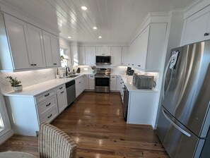 A modern kitchen with white cabinetry, stainless steel appliances, and a wooden floor. - Best View on Lake Murray in Chapin (Chapin)
