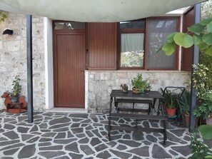 A stone-tiled patio with a wooden door, a window with blinds, and a table with potted plants.