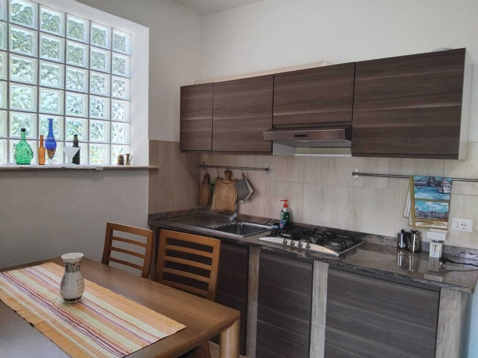 Una cucina compatta con mobili in legno scuro, un fornello a gas, un lavello e una finestra con bottiglie decorative.