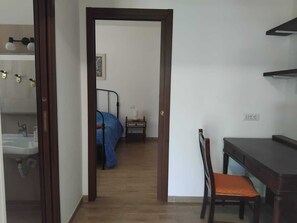 A room with a bed, a desk, a chair, and a bathroom visible through an open door.