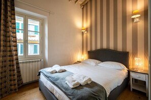 A hotel room with a bed, two bedside lamps, a window with curtains, and a radiator. - Appartamento di charme (Florence)