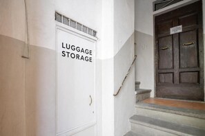A white door labeled 'LUGGAGE STORAGE' with a metal handle, next to a set of stone steps leading to a dark wooden door with a sign above it. - Appartamento di charme (Florence)