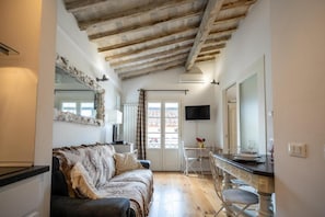 A room with a sofa, a dining table with chairs, a TV mounted on the wall, and a window with a view. - Appartamento di charme (Florence)