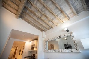 A room with a high ceiling, exposed wooden beams, a large mirror with a distressed frame, and a view into an adjacent room. - Appartamento di charme (Florence)