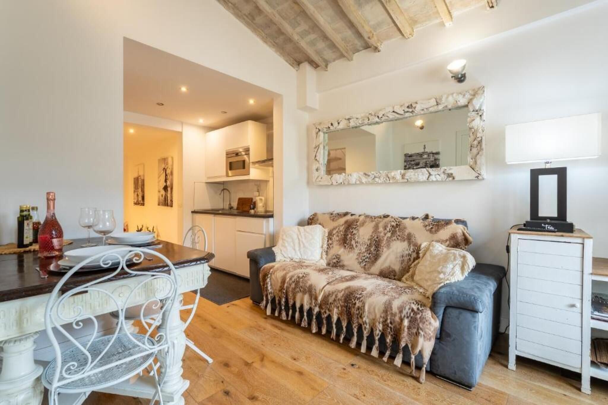 A cozy living room with a sofa, a dining table with chairs, a kitchen area, and a television on a stand.