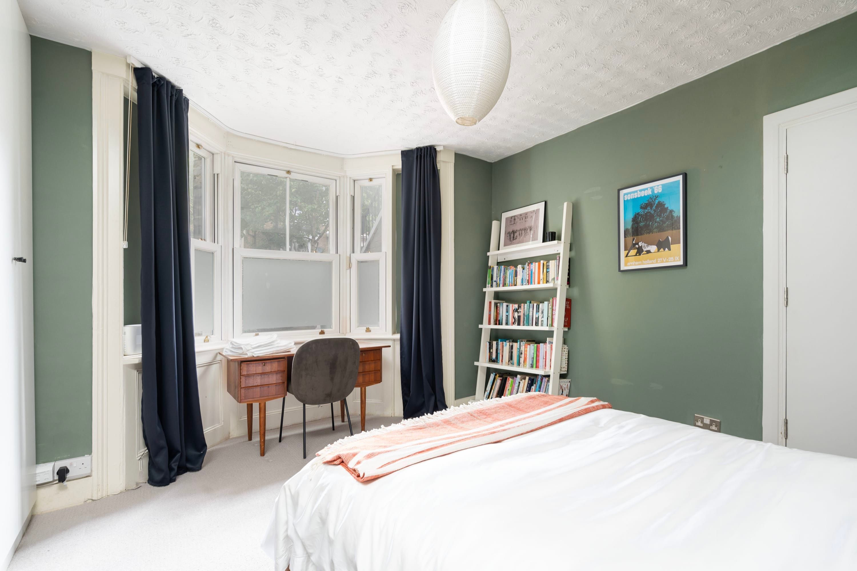 A bedroom with a bed, a desk, a chair, a bookshelf, and a window.