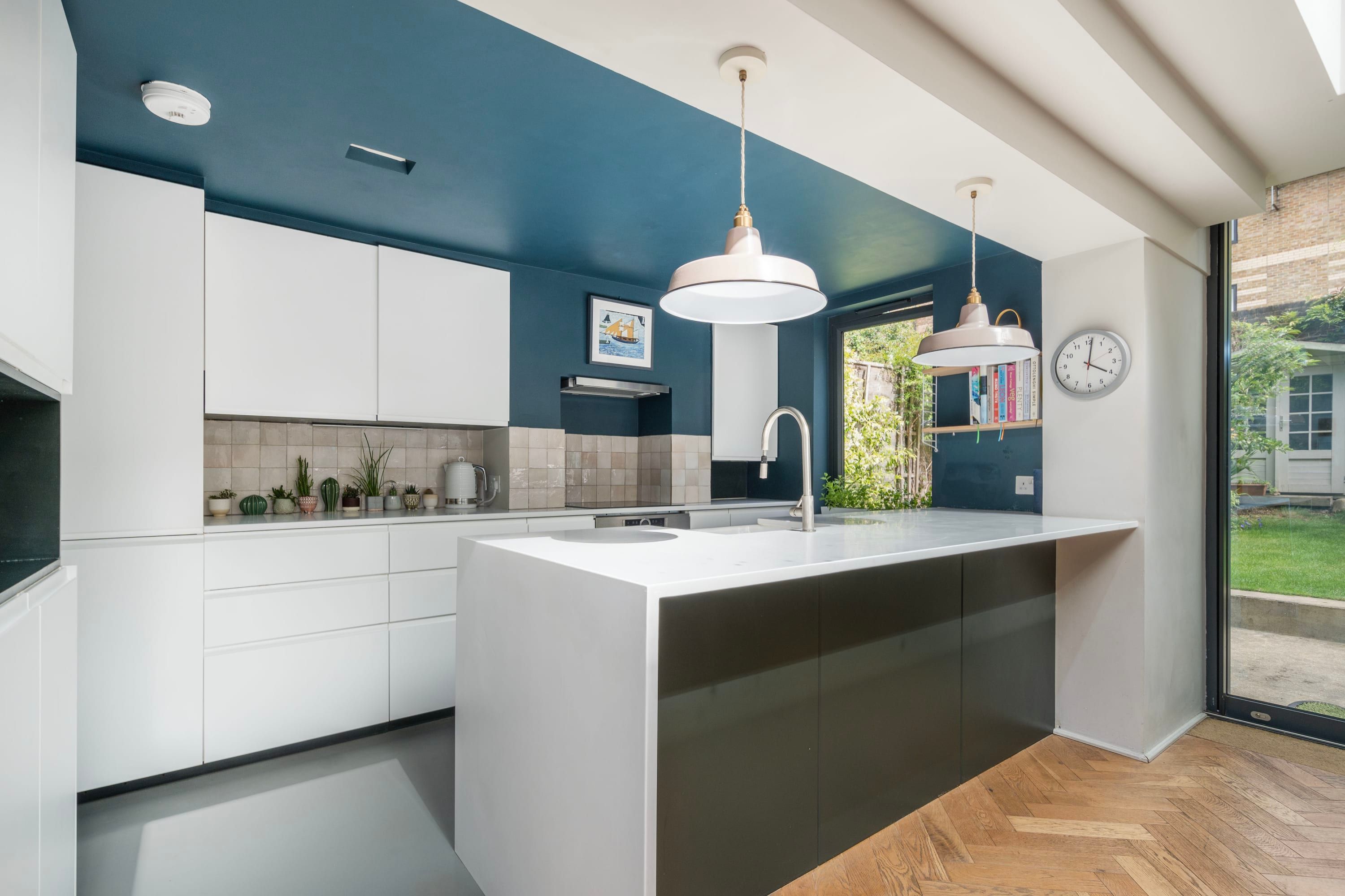 Een moderne keuken met een centraal eiland, witte kasten en hanglampen.