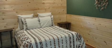 A room with a bed, a ceiling fan, a small window, and a decorative wall hanging.