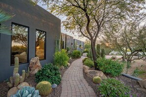 A modern building with large windows and a paved pathway leading to a garden with cacti and shrubs. - Saguaro Sanctuary (Cave Creek)
