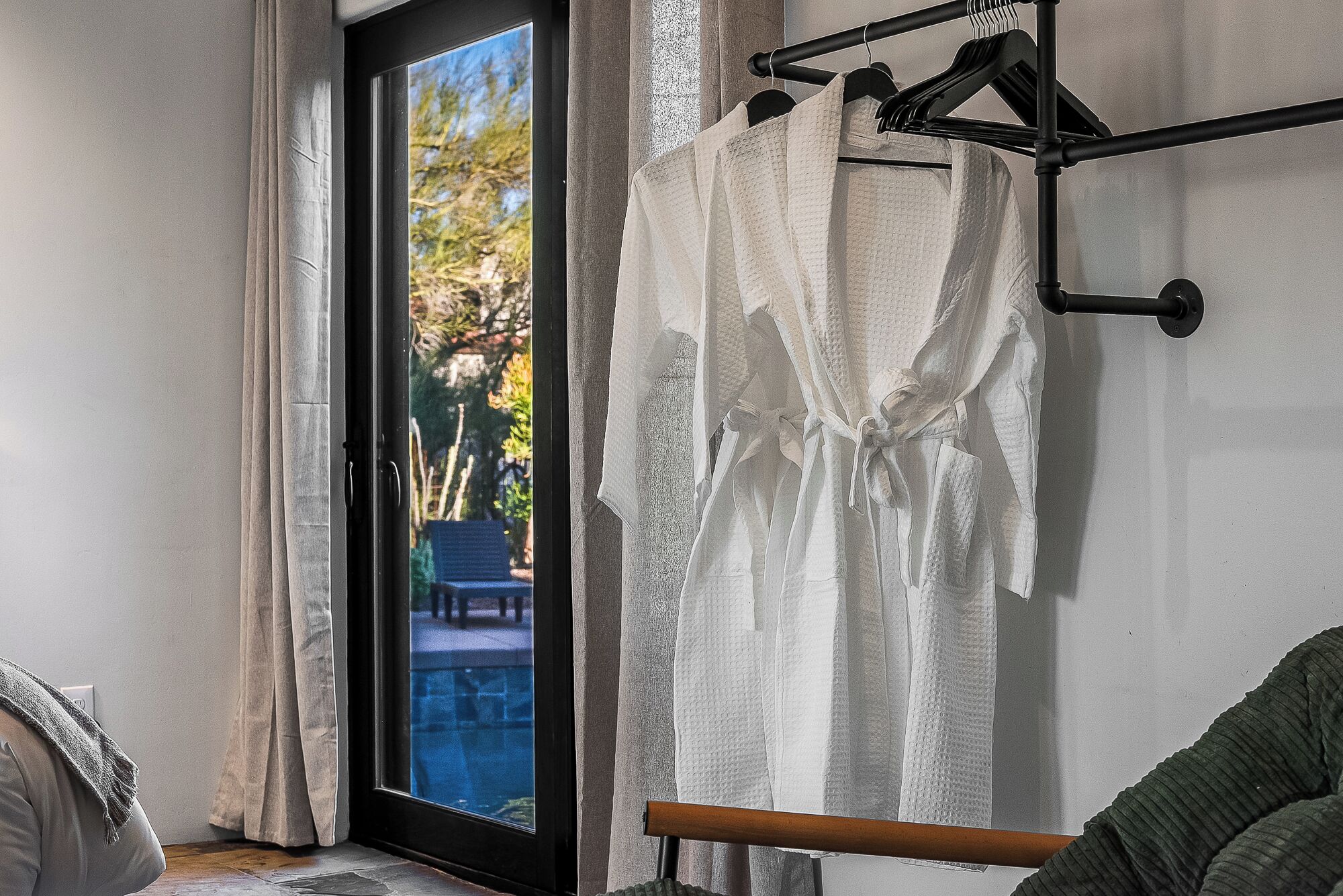 A room with a sliding glass door leading to a balcony, a wooden chair, and a rack with white towels.