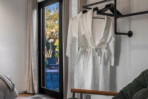 Una habitación con una puerta corrediza de vidrio que da a un balcón, una silla de madera y un perchero con toallas blancas.