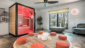 A modern living room with a large glass cabinet, a ceiling fan, a large window with a view of cacti, and several round orange ottomans. - Saguaro Sanctuary (Cave Creek)