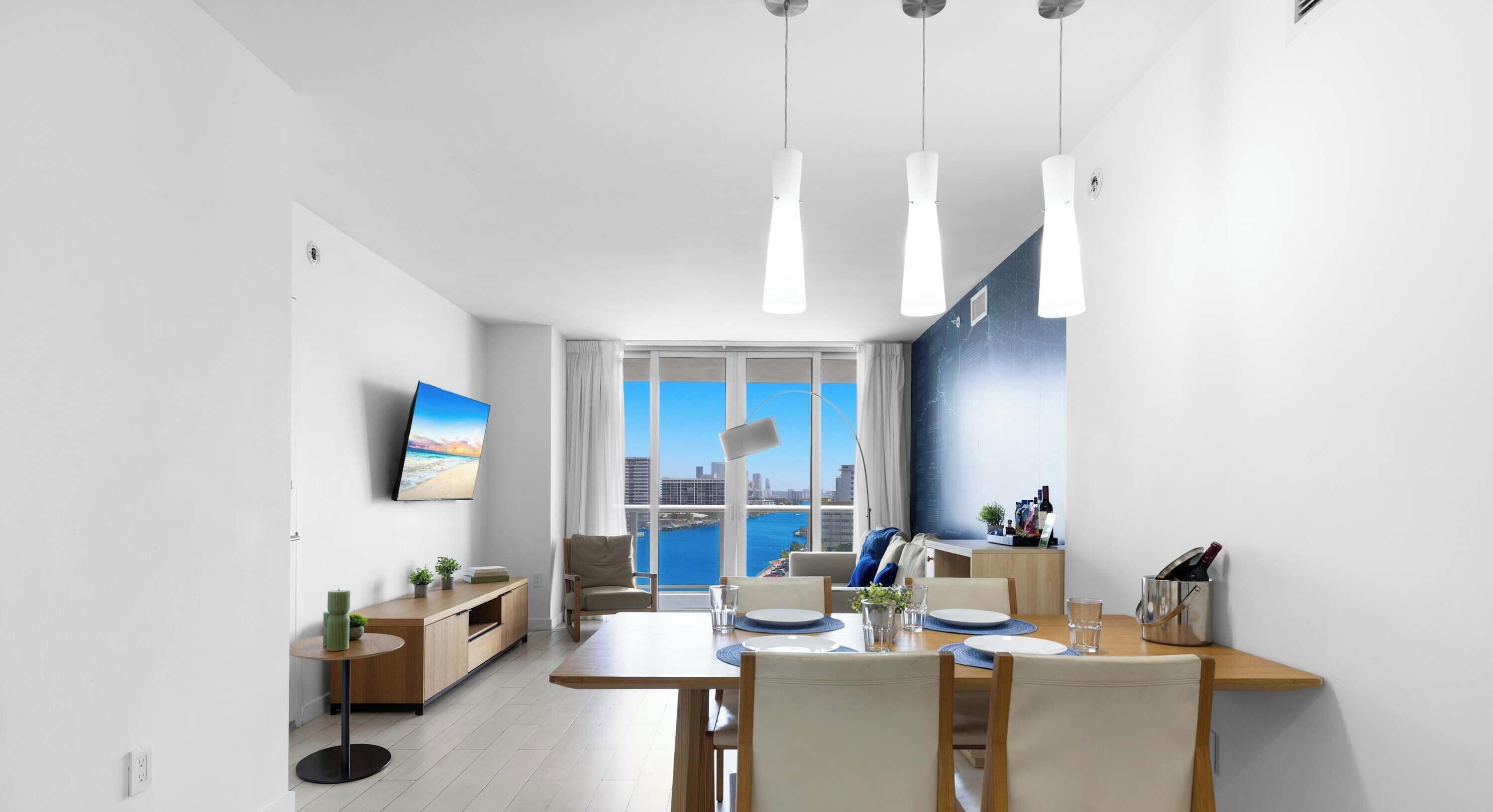 A modern dining area with a view of the sea, a flat-screen TV, and a dining table set for four.