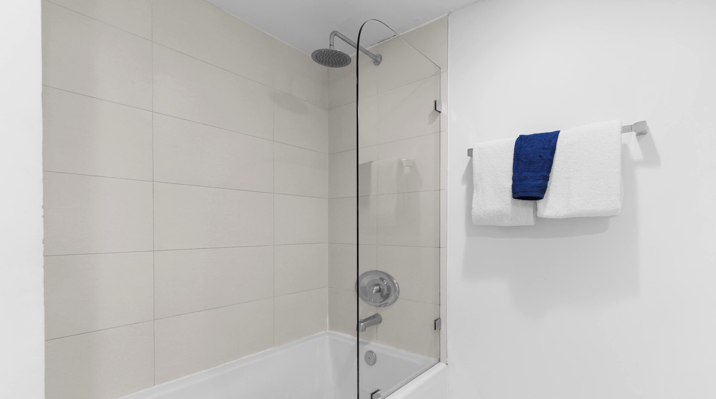 Eine Dusche mit Glastür, eine weiße Fliesenwand und ein blaues Handtuch an einem Haken.