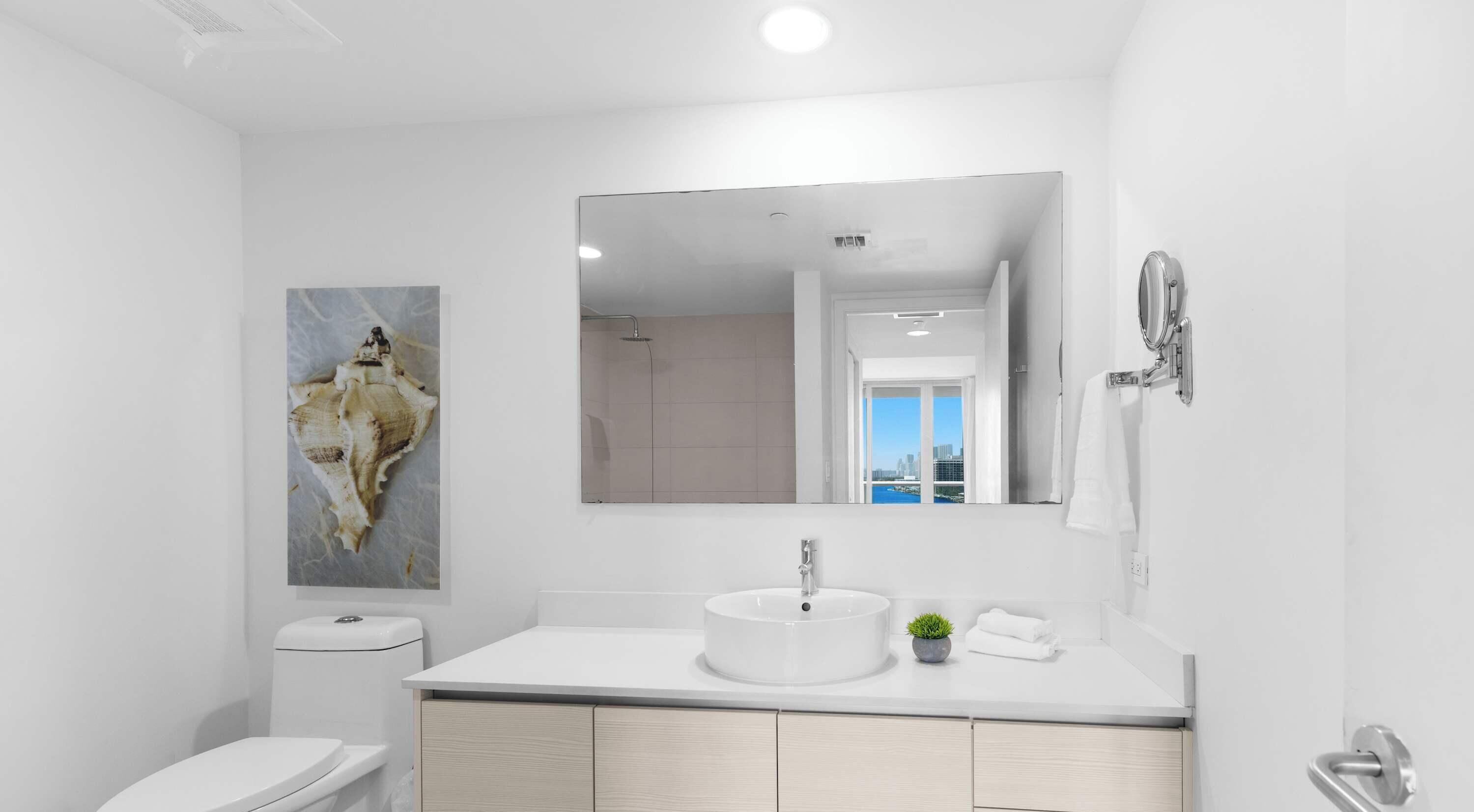 Une salle de bain moderne avec un lavabo blanc, des toilettes et un grand miroir.