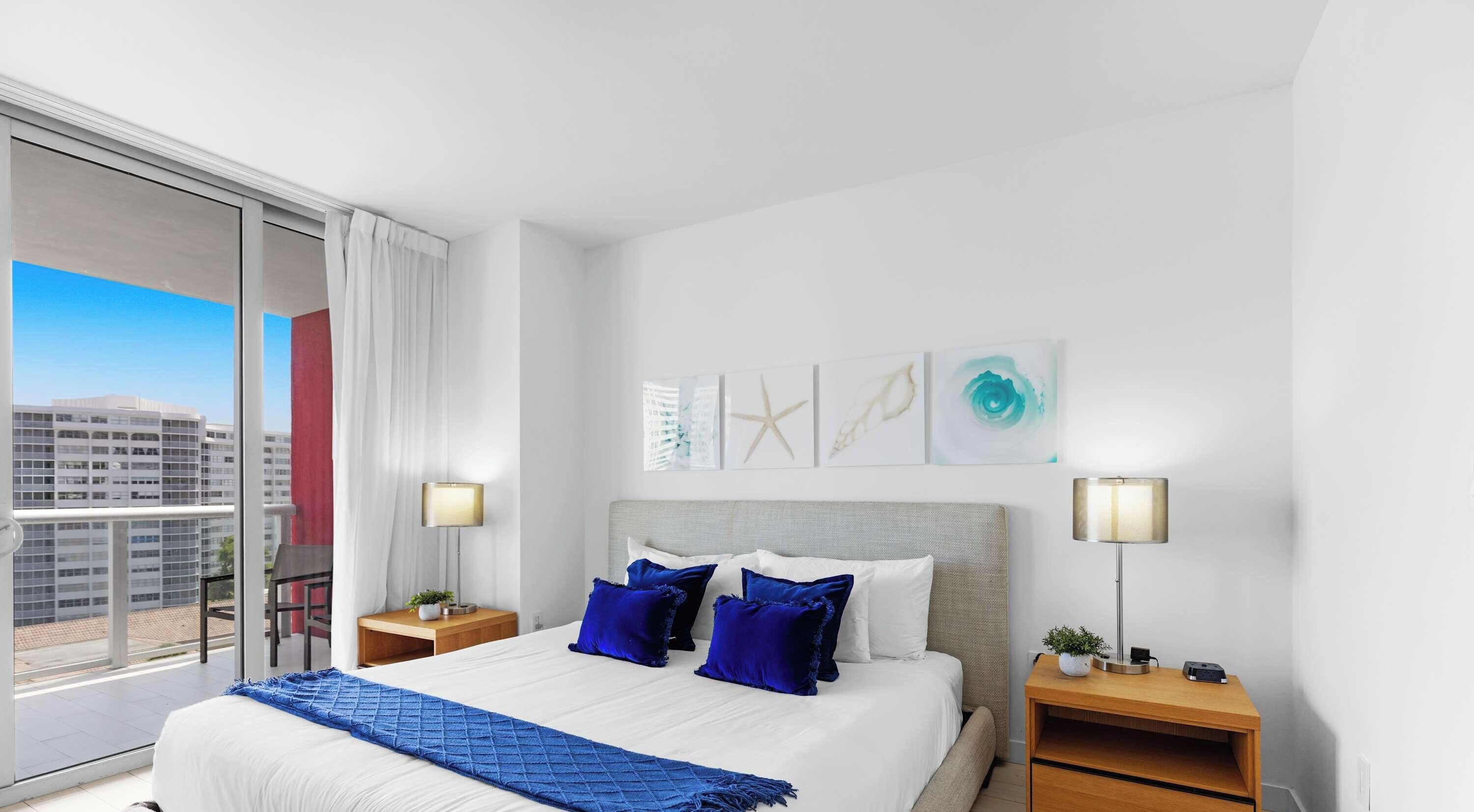 Een hotelkamer met een groot bed, twee nachtkastjes, uitzicht op de stad en kunst aan de muur.