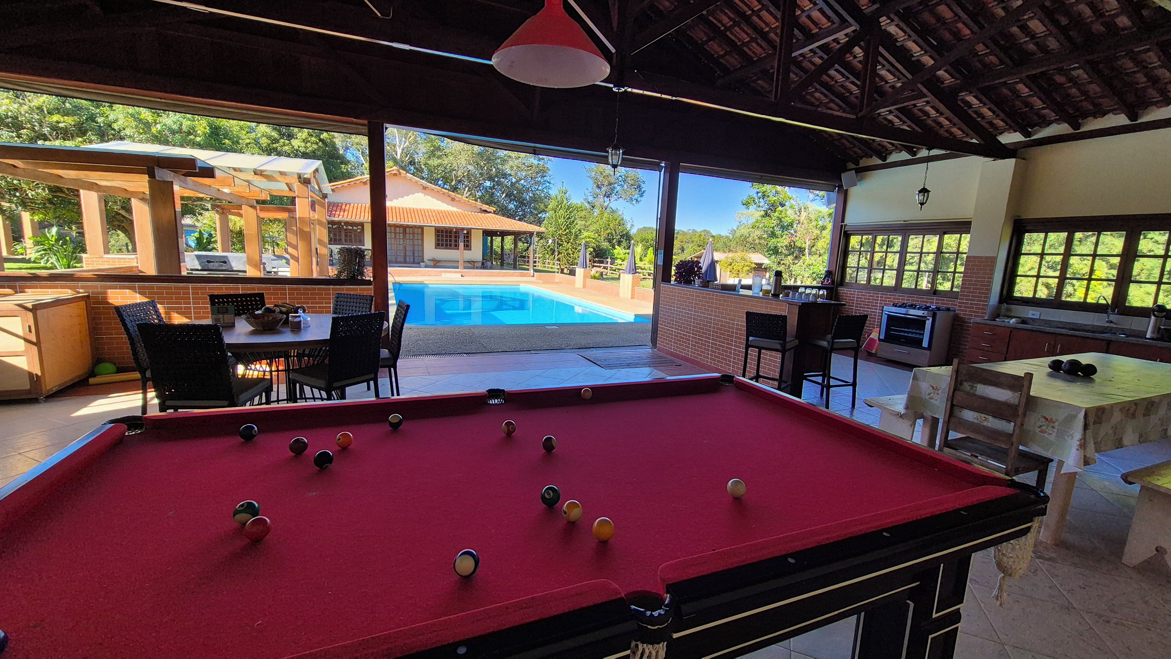 Mesa de bilhar com bolas, área de refeições com cadeiras e uma mesa, e vista para uma piscina e uma casa.