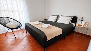 A bedroom with a bed, a chair, a bedside table with a lamp, and a wall socket. - Playa & Golf Townhouse - 2 min from MAJ Golf Academy (Torremolinos)