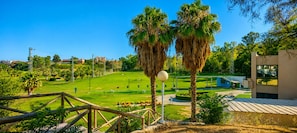 A golf course with a wooden fence, palm trees, and a modern building in the background. - Playa & Golf Townhouse - 2 min from MAJ Golf Academy (Torremolinos)