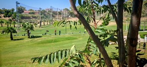 A golf course with a clear sky, palm trees, and distant buildings. - Playa & Golf Townhouse - 2 min from MAJ Golf Academy (Torremolinos)