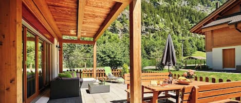 A wooden deck with outdoor seating, a table with food, and a mountain backdrop.