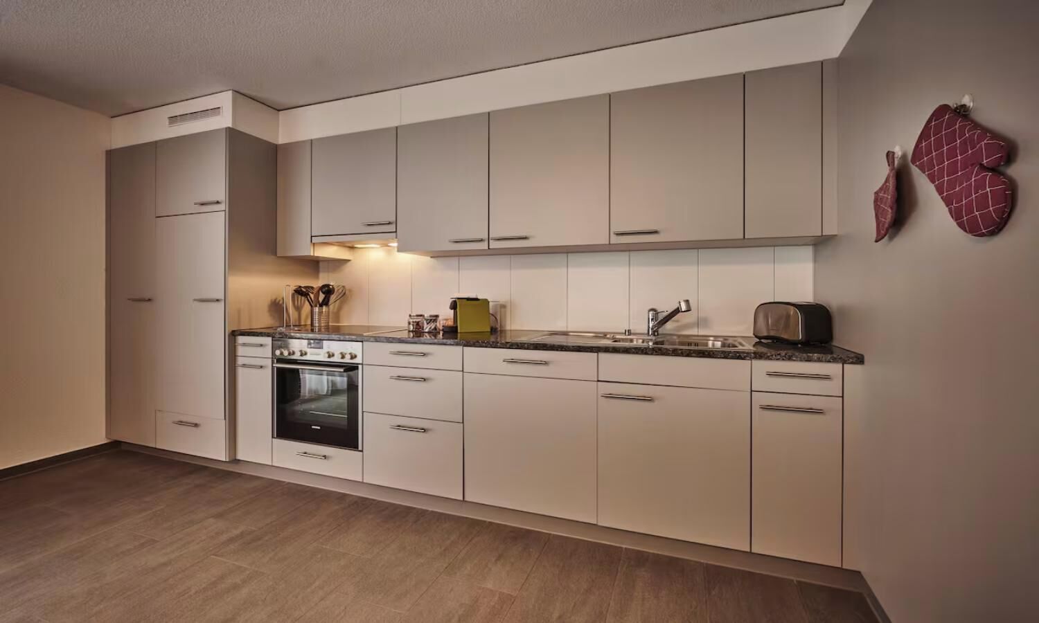 Una cocina moderna con armarios blancos, horno empotrado y encimera con un tostador.