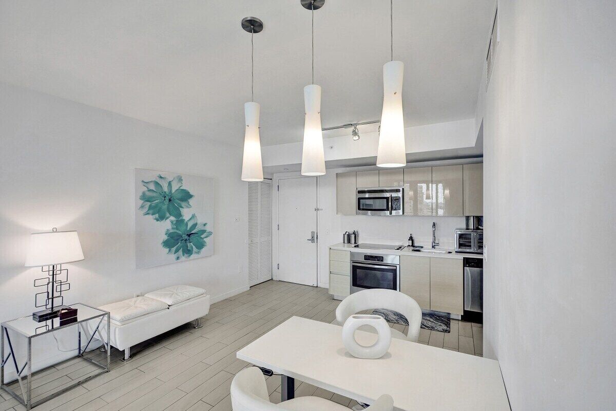 Une cuisine moderne dotée d’appareils électroménagers en acier inoxydable, un coin repas avec une table et des chaises blanches, ainsi qu’un banc blanc.