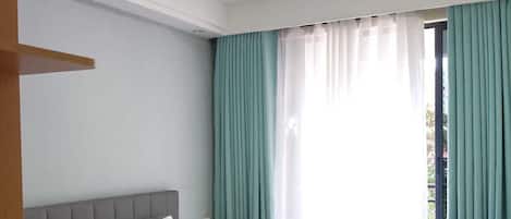 Quarto com cama, janela com cortinas e vista para o exterior.