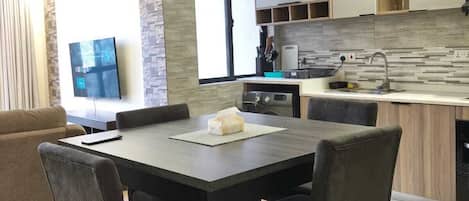 A modern kitchen with a dining area, a television, and a sofa.