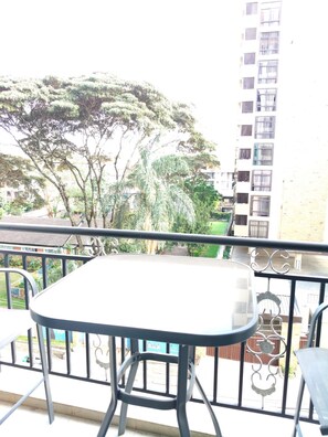 Ein Balkon mit Tisch und Stühlen, der auf einen Wohnbereich mit Bäumen und einem hohen Gebäude blickt.