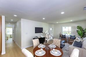 A modern living room with a dining area, a flat-screen TV mounted on the wall, and a large plant. - Modern 3BR Monterey Park Home Near LA & DTLA (Monterey Park)