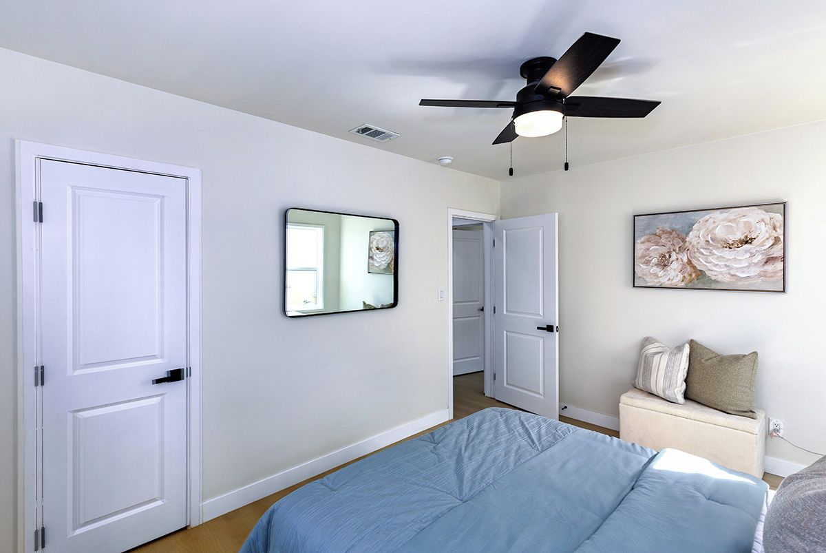 A bedroom with a bed, a ceiling fan, a door, and a wall-mounted mirror.