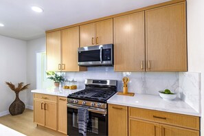 Une cuisine dotée de meubles en bois, d’un four à micro-ondes en acier inoxydable, d’une cuisinière à gaz et d’un plan de travail en marbre.