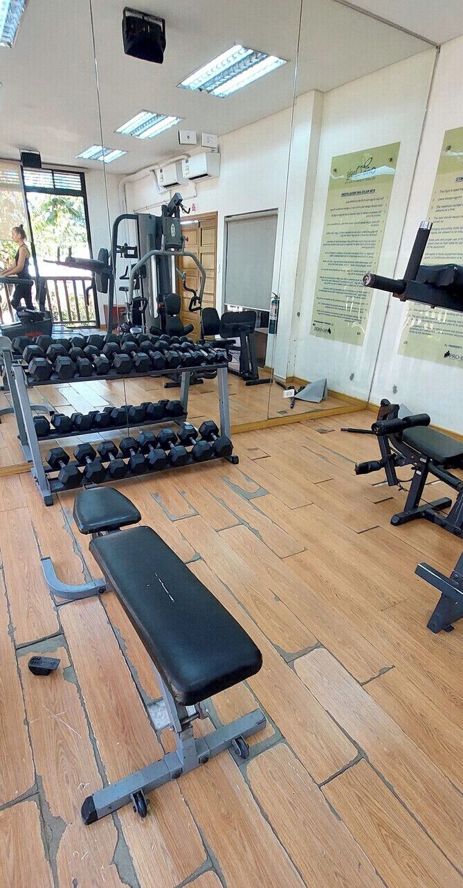 Ein Fitnessstudio mit Trainingsgeräten, Bänken und einer Spiegelwand.