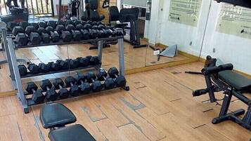 Ein Fitnessstudio mit Trainingsgeräten, Bänken und einer Spiegelwand.