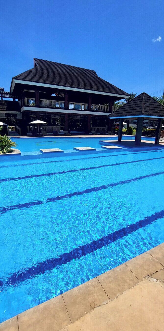 A swimming pool with clear blue water, surrounded by a building with a balcony and a gazebo.
