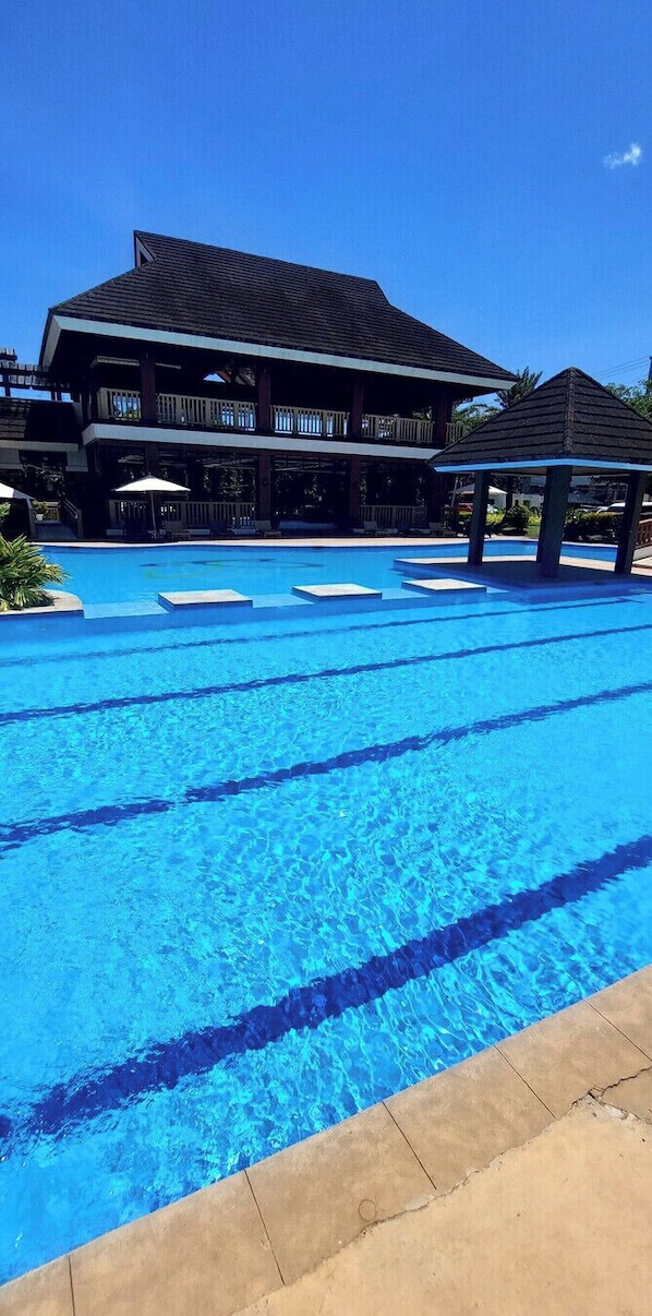 Una piscina con agua azul cristalina, rodeada por un edificio con balcón y un pabellón.
