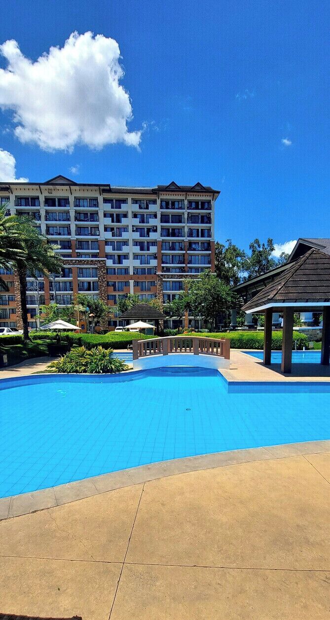 Une piscine, un ciel d’un bleu limpide, un hôtel à plusieurs étages et un kiosque.