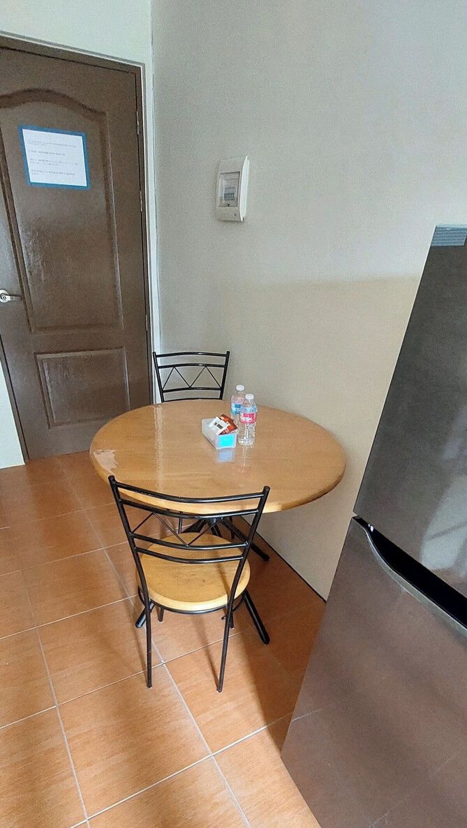 Un petit coin repas avec une table ronde, deux chaises, un réfrigérateur et une porte sur laquelle est affiché un avis.