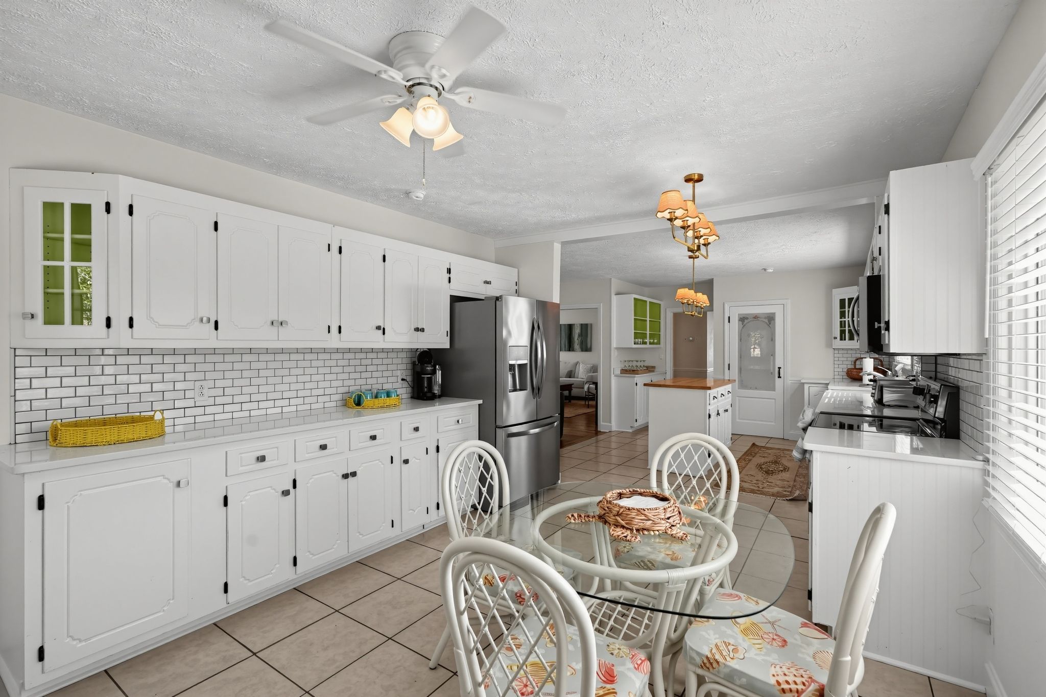 A modern kitchen with white cabinetry, a stainless steel refrigerator, a dining table with chairs, and a ceiling fan.